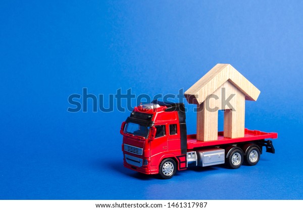 A red truck transports a wooden house. Concept\
of transportation and cargo shipping, moving company. Construction\
of new houses and objects. Industry. Logistics and supply. Move\
entire buildings.
