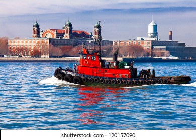 Red Tugboat Passing In Front Of Historic Ellis Island In The New York City Harbor.