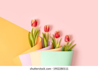 Red tulip flowers in a bouquet made of colorful wallpaper arange in diagonal. Creative background spring concept.