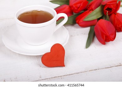 Red tulips, red heart and cup of tea on white wooden table. Romantic valentines day background. Love view 