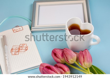red tulips, a notebook with a coffee mug on a blue background, and a photo frame. Flat lying, top view.