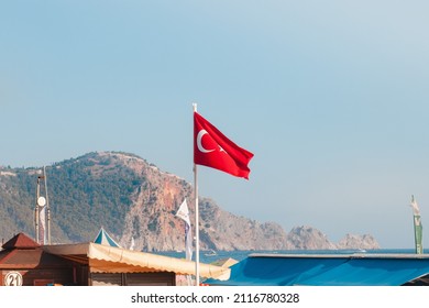 A Red Turkey Flag On A Pole Near A Beach. Mountain In The Background. Sunny Day. Turkey, Alanya