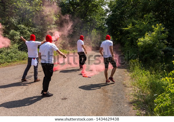 red ultras\
fans with torches and smokes make an ambush on the street.\
hooligans with red head masks close the\
road.