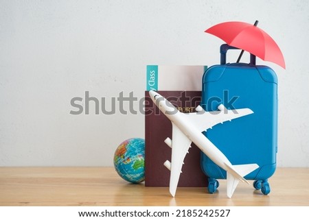 Red umbrella cover airplane, passport, flight tickets and suitcases travelers on wooden background. Travel insurance covers loss suitcase, flight delays, cancellations, accident and medical expenses.