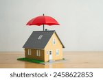 Red umbrella cover home model on wooden table with white background copy space. House, real estate, property insurance business, mortgage loan insurance concept. Insurance is risk control management.