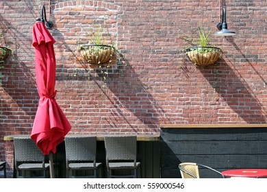 Red Umbrella Folded Up Against A Brick Wall In A Patio Setting