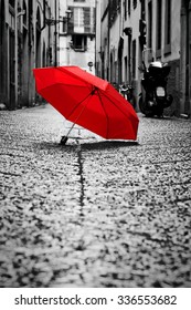 Red Umbrella On Cobblestone Street In The Old Town. Wind, Rain, Stormy Weather. Color In Black And White Conceptual, Idea. Vintage, Retro Style.