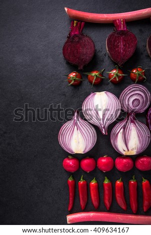 Red vegetables cut in halves, flat lay design on dark background, symmetric.