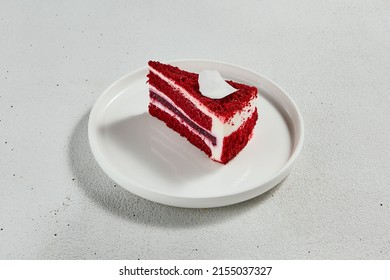 Red velvet cake on white ceramic plate. Minimal composition with piece cake. Popular dessert - red velvet with cheese cream and chocolate sponge. Red velvet in minimal style