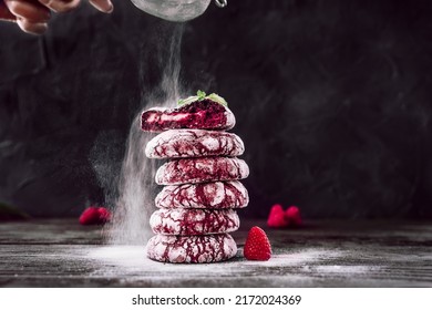 Red velvet cookies. Chefs hands with small sieve for baking sprinkling powdered sugar. Baker decorating and sprinkling stack of cookies. Dark background, homemade bakery goods, colourful food