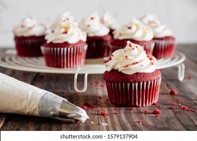 Red velvet cupcakes on a cooling rack and a pipping bag on a rustic wooden table - Powered by Shutterstock