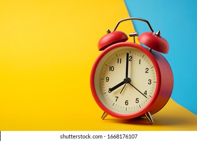 Red vinatge alarm clock show 8 o'clock with yellow and blue background.