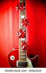 A Red Vintage Solid Body Electric Guitar With Red Ribbon Bows On Fretboard. A Concept Image For Christmas And Holiday Season Music Event.