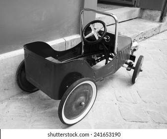 Red Vintage Toy Car Near Entrance To The House. Back And Side View. Aged Photo. Black And White.