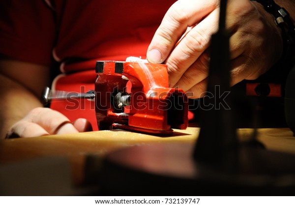 Red vise and hands of handy man working in\
workshop with workbench\
