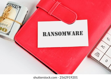 A red wallet rests next to a stack of hundred dollar bills, with a card reading ransomware laid atop. This setup highlights issues of cybersecurity and financial risk management today.