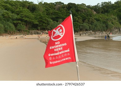 Red warning flag displaying no swimming instructions in multiple languages at a public beach. Editorial image illustrating beach safety, coastal regulations and tourist information.