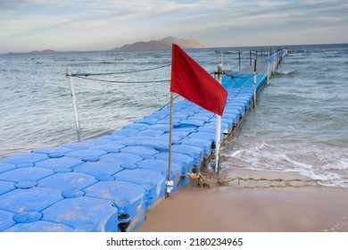 Red Warning Flag On Beach. Blue Plastic Pontoon In Sea Water. Swimming Forbidden In Windy Weather, Ocean Waves, Storm