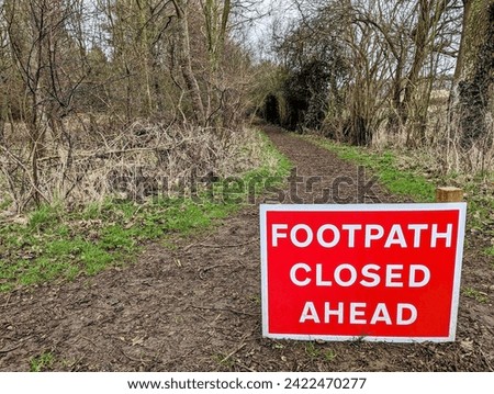 Red warning sign in the countryside by a woodland path reads Footpath Closed Ahead