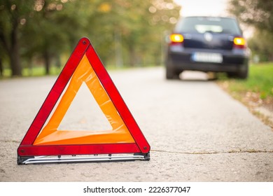 Red warning triangle with a broken down car. Emergency triangle on the road, stopped car.