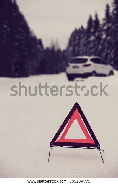 The red warning triangle laid out the road to\
warn of the accident in Finland. Focal point is a warning triangle.\
White car and the background out of focus. Image includes a vintage\
effect.