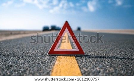 A red warning triangle is positioned on a paved road, centered on a bright yellow line, indicating a hazard or breakdown.