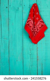 Red western bandana or handkerchief hanging on blank antique rustic teal blue old weathered background; bandanna