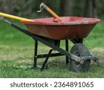 red wheelbarrow cart with garden tools inside (rake, shovel, handles sticking out) dirty yard work