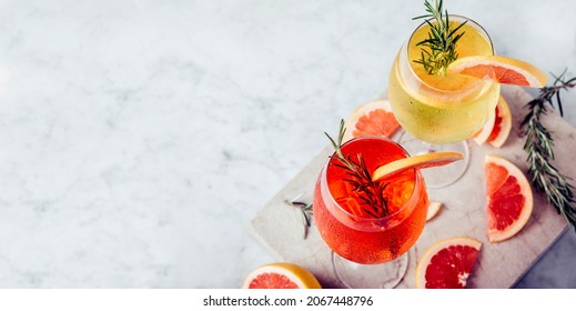 Red and white aperol spritz garnish in wine glasses with rosemary and grapefruit on luxury marble table. Bitter alcohol cocktail in wineglass. Top view. Happy hour restaurant menu banner.
