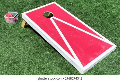 Red And White Bean Bag Toss Cornhole Game On A Green Turf Field.