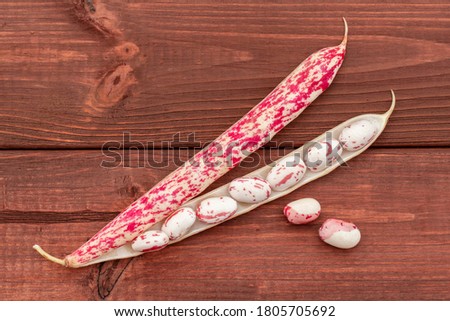 Red and white beans from inside red string bean pod on a wooden background