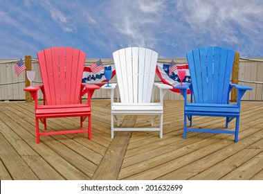 Red, White And Blue Adirondack Chairs On Wooden Deck With American Flags