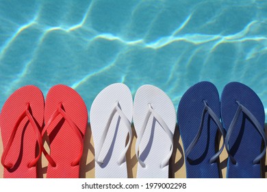 Red white and blue flip flops sitting on the edge of a swimming pool.