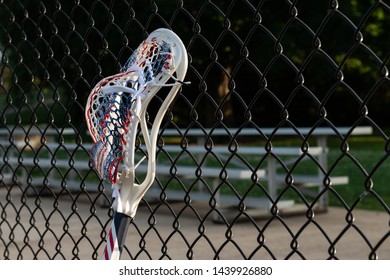 Red, White, And Blue Mens Lacrosse Stick Leaning Against A Chain Link Fence.