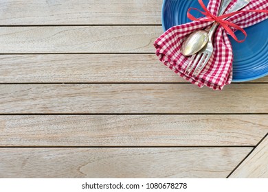 A Red White And Blue Picnic Table Place Setting With Napkin, Fork And Spoon And Plate In An Upper Corner On Horizontal 
Wood Board Table Top Background With Room Or Space For Copy, Text Or Your Words.