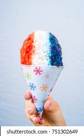 Red, White And Blue Snow Cone In Paper Cone And Blue Straw Held By Female Hands.