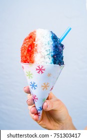 Red, White And Blue Snow Cone In Paper Cone And Blue Straw Held By Female Hands.