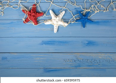 Red White And Blue Starfish In Nautical Netting On Blue Rustic Wood