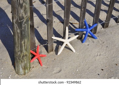 Red, White And Blue Starfish Sitting By Beach Fence. Room For Your Text