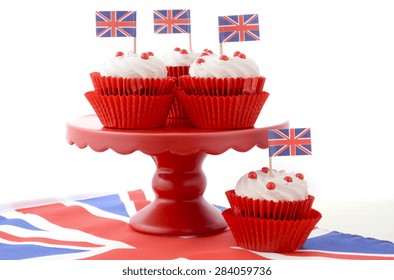 Red White And Blue Theme Cupcakes On Red Cake Stand With UK Union Jack Flags On White Wood Table For Queens Birthday And Great Britain Party Food. 