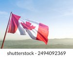 A red and white Canadian flag is flying in the sky. The flag is waving in the wind and is positioned on a hill. Concept of patriotism and pride in Canadian identity