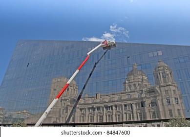 A Red And White Cherry Picker And Glass Building With Reflection Of Historic Building