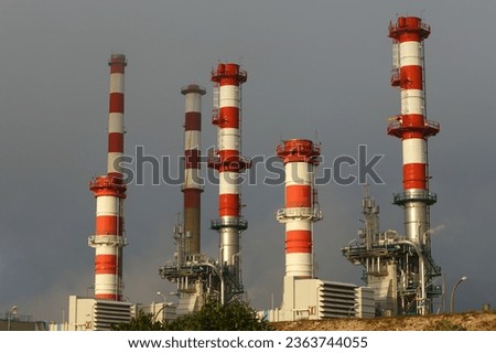 Red and white chimneys from part of a big oil refinery and powerplant at sunset