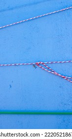 Red And White Cord And Green Plastic Bridle Tied In Blue Stucco Pillar