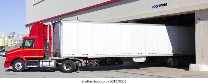 Red And White Delivery Semi Backing Into Warehouse Loading Bay.