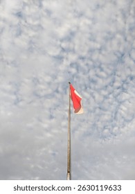 Red and white flag under white clouds