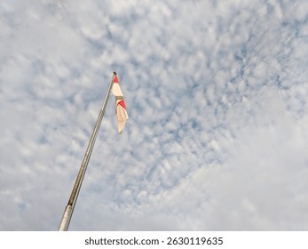 Red and white flag under white clouds