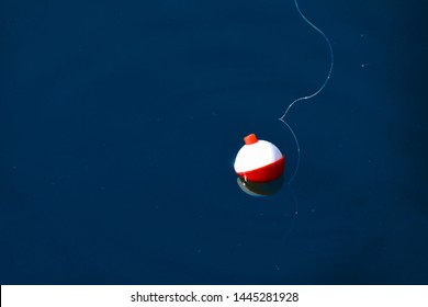 Red And White Floating Fishing Bobber With White Fish Line On Dark Blue Still Water