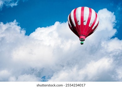 Red and white hot air balloon on the background of bright blue cloudy sky.