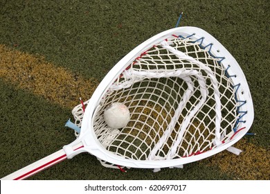 A Red And White Lacrosse Goalie Stick On A Green Turf Field With A Ball In The Net